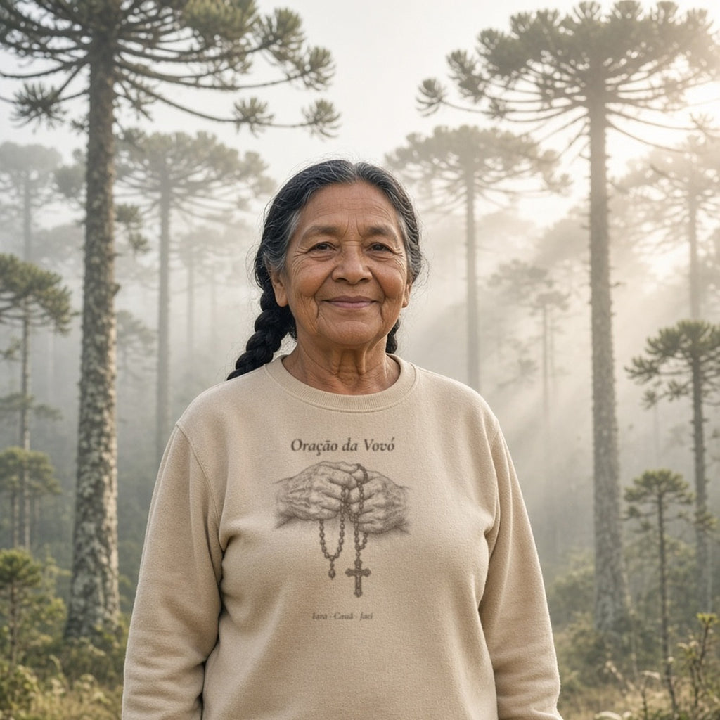 Avó indígena de trança em um bosque de araucárias com neblina vestindo o Suéter Oração da Vovó areia com os nomes de 3 netos, personalizada com os nomes dos netos